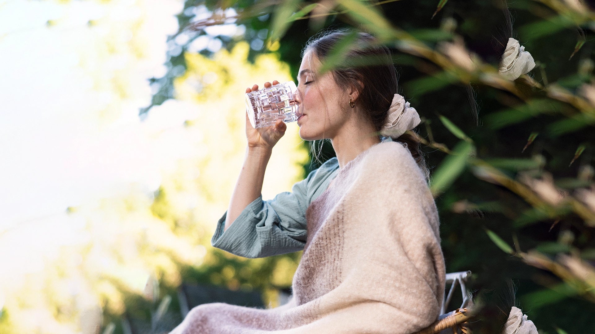Woman drinking a glass of water sitting in greenery.