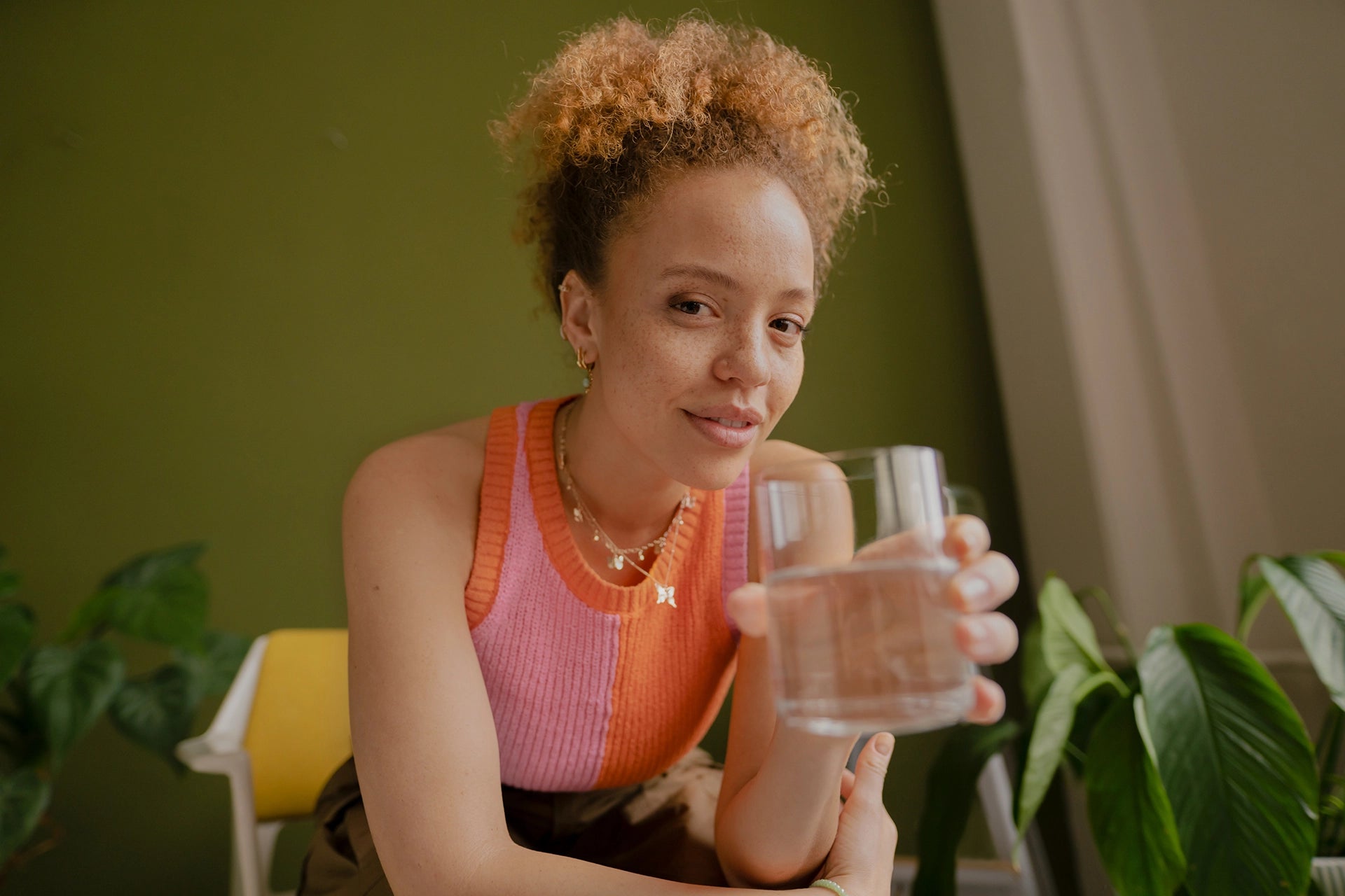 Person holding a glass of water while seated indoors.