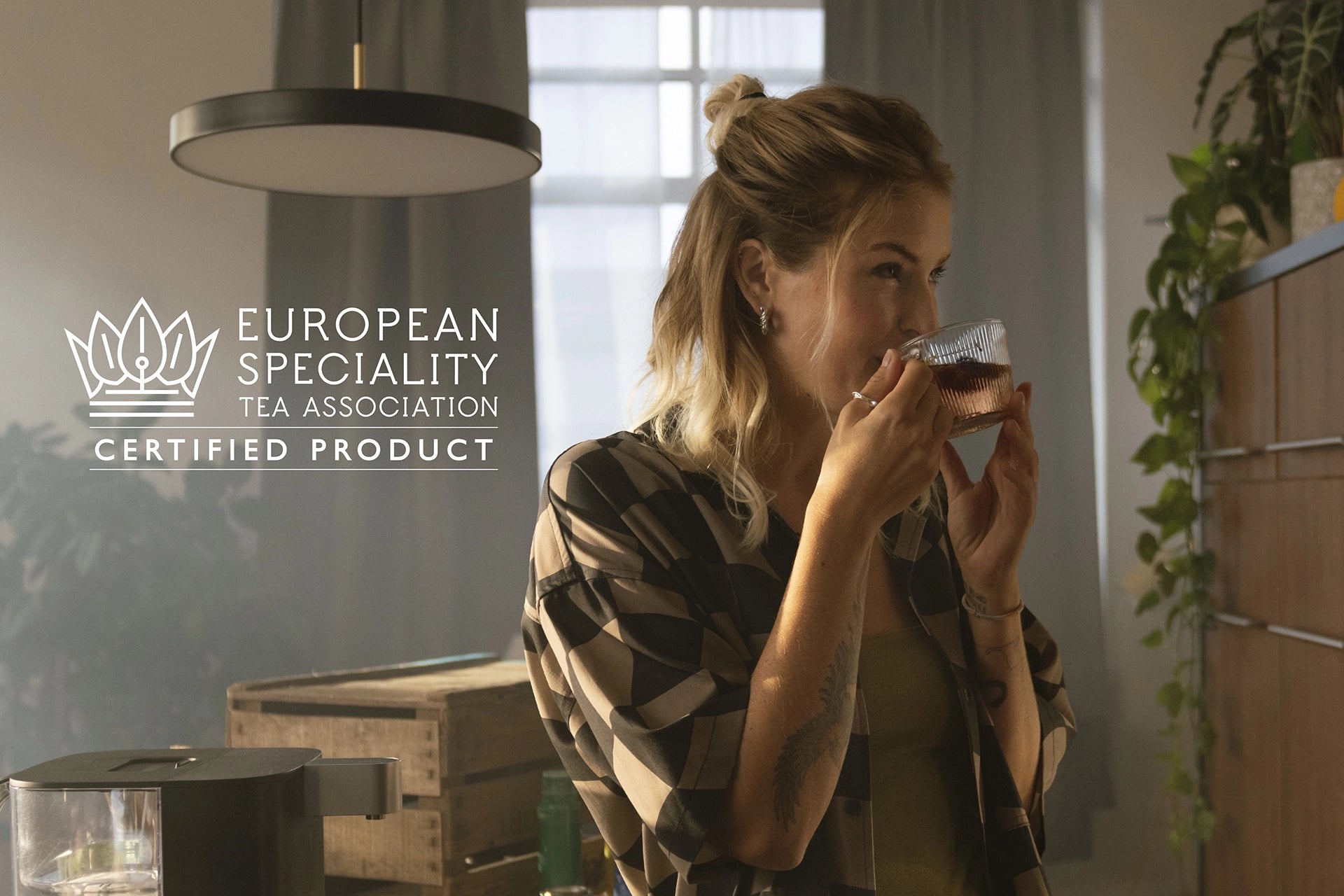 Woman drinking tea with white ESTA logo on image.