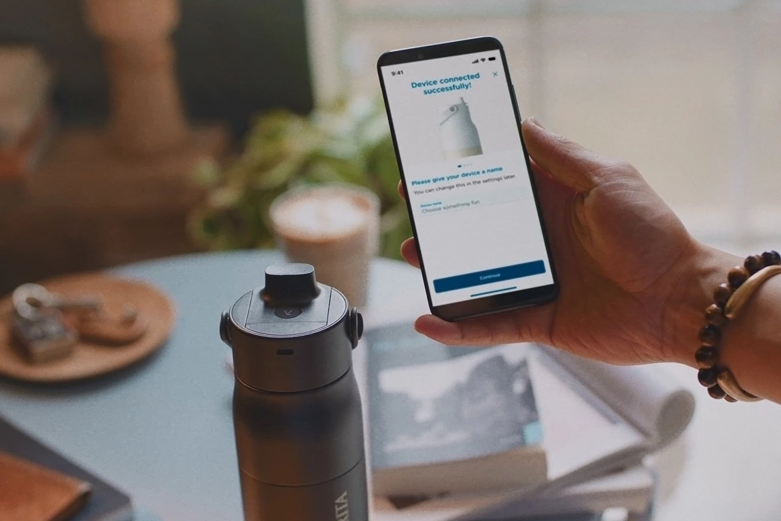 BRITA LARQ iQ Filter Bottle next to a smartphone displaying the BRITA app during setup.