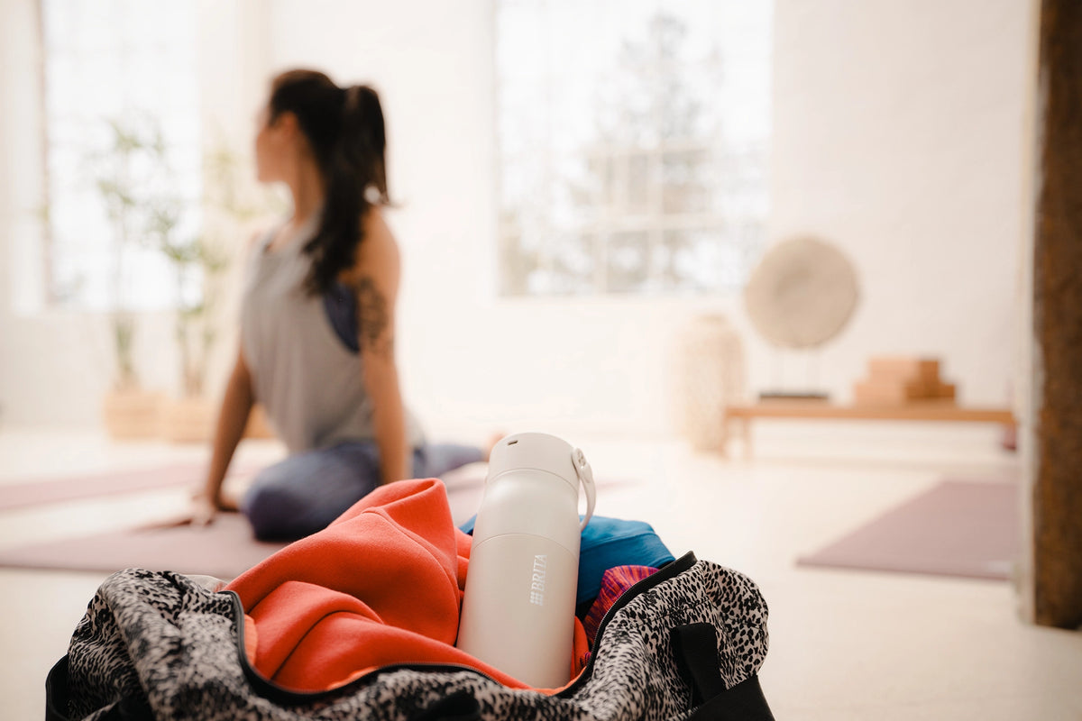Beige BRITA LARQ bottle placed in a gym bag beside a yoga mat in a yoga studio.