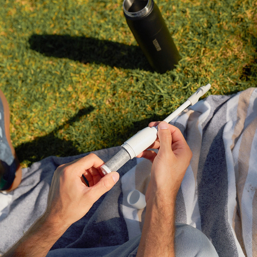 A person sitting on grass outdoors inserting BRITA LARQ filter in BRITA LARQ filter kit.