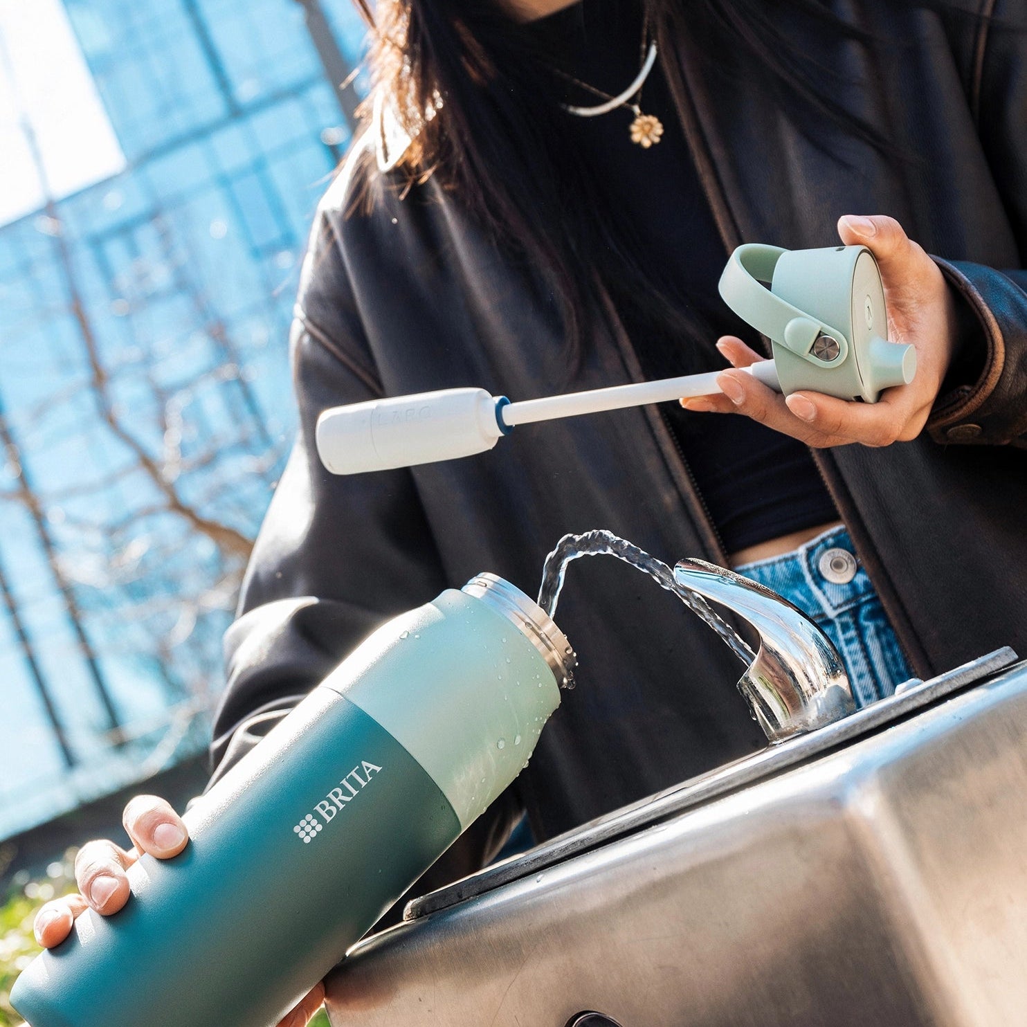 Green BRITA LARQ Bottle iQ being refilled with water in an outdoor setting