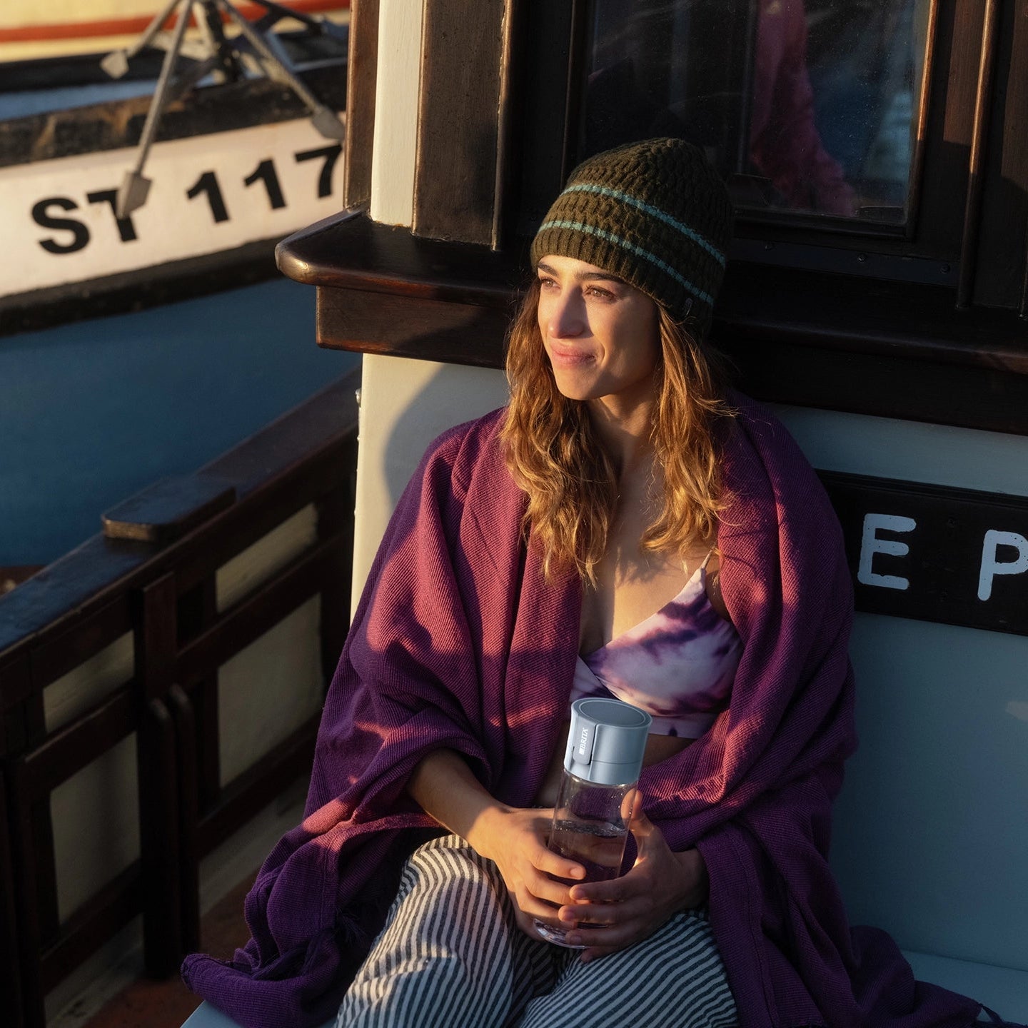 Woman sitting on a boat holding BRITA water filter bottle Model Vital, with another boat visible in the background.