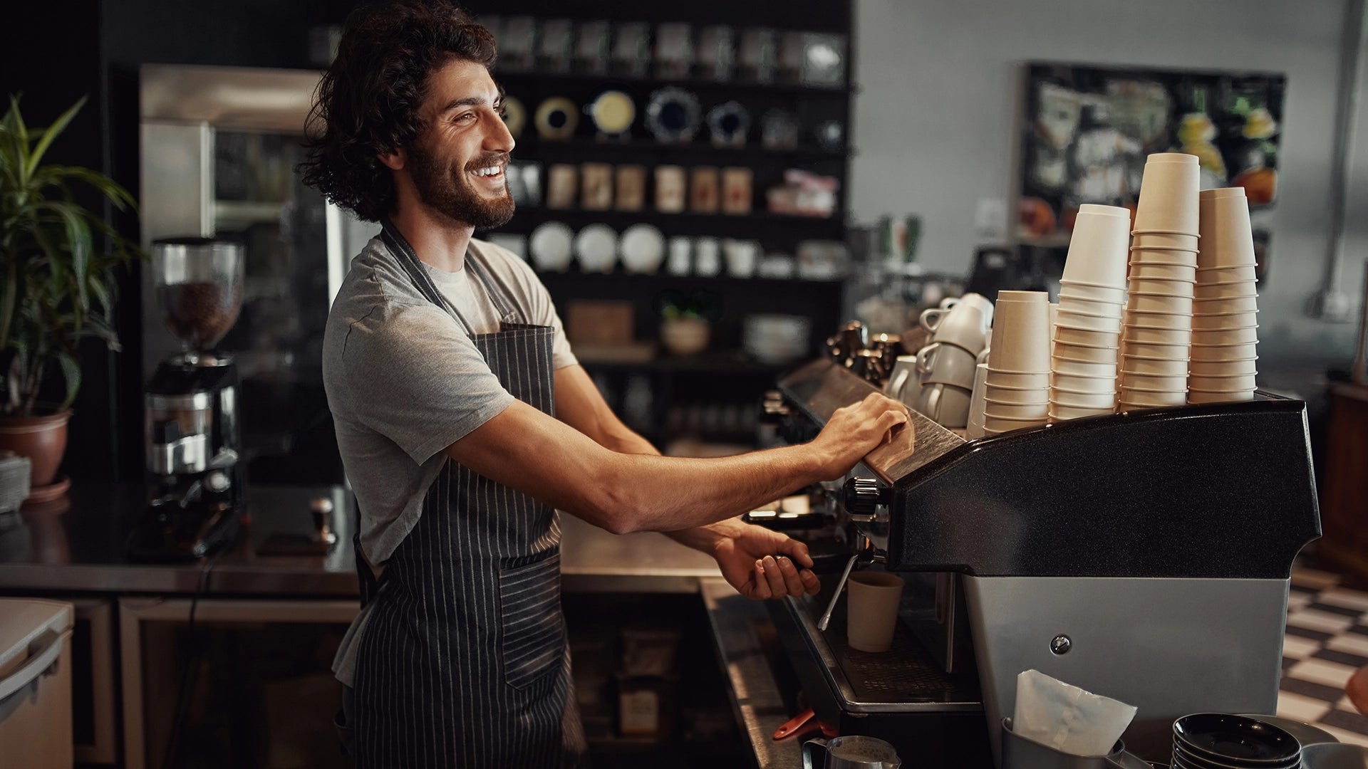 Barista at work in a coffee shop with stacks of cups on the counter.