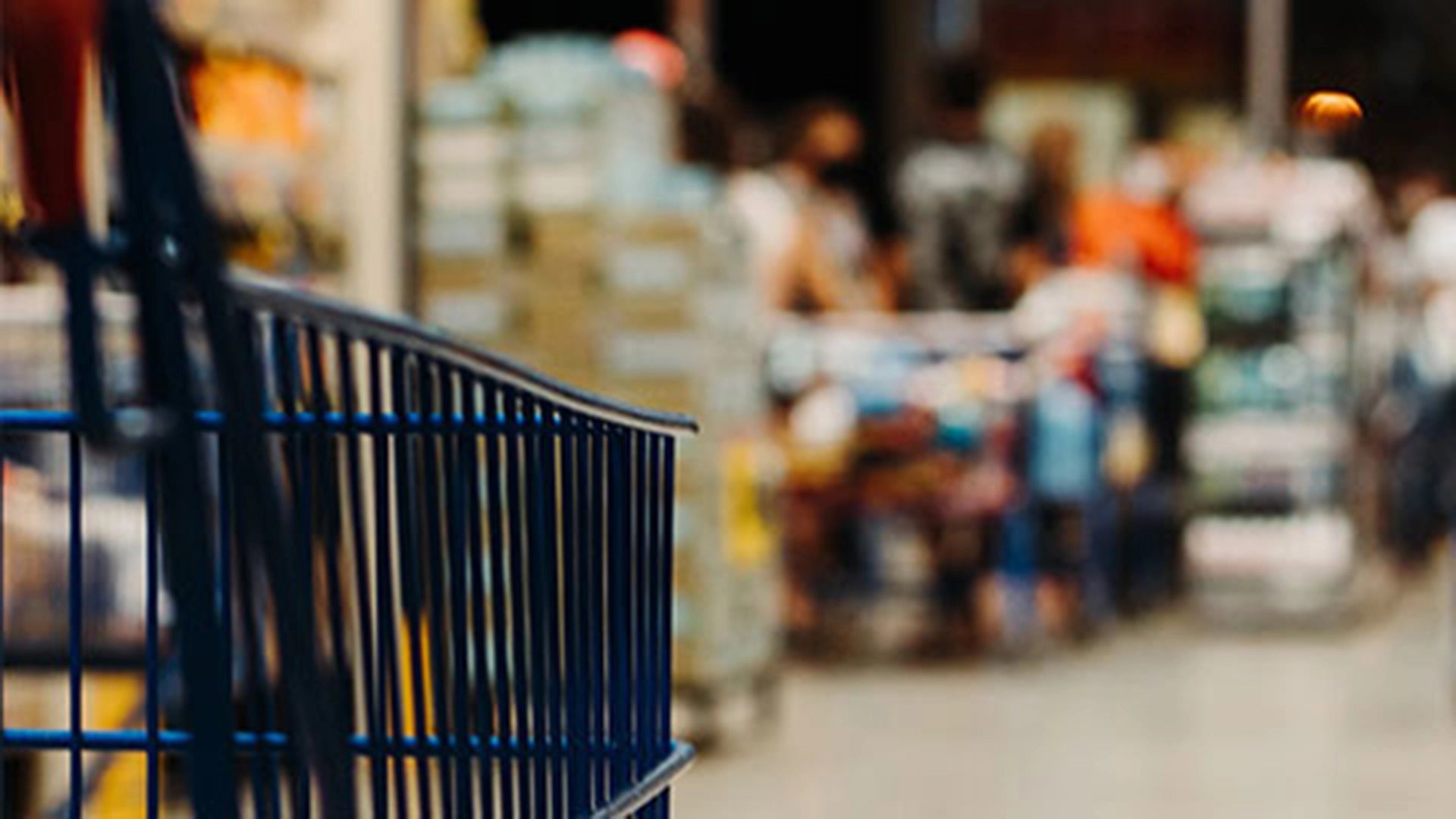 Blurry image of a shopping cart in a store with people in the background.
