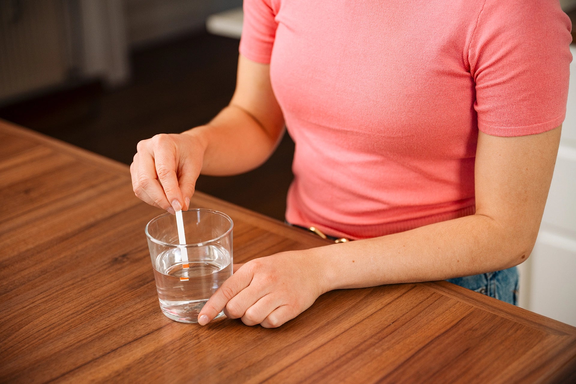Person testing water hardness with a test strip in a glass of water on a wooden table.