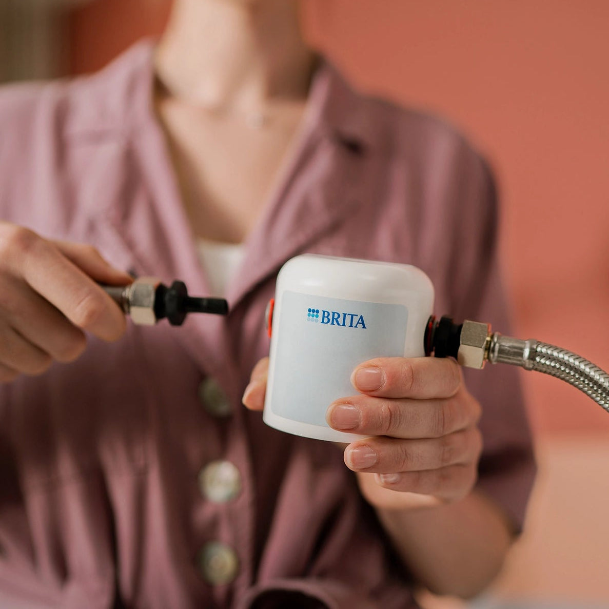 Installation of a BRITA replacement part with connected water hose fittings.