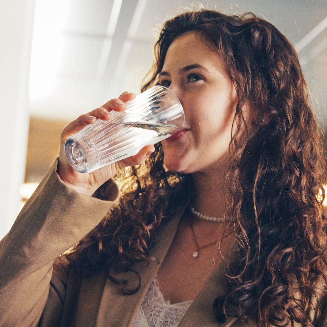 Una donna che beve acqua in casa con lo sfondo sfocato