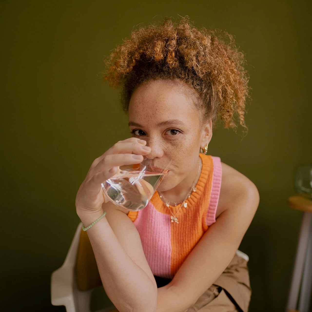 Person holding a glass of water against a green background