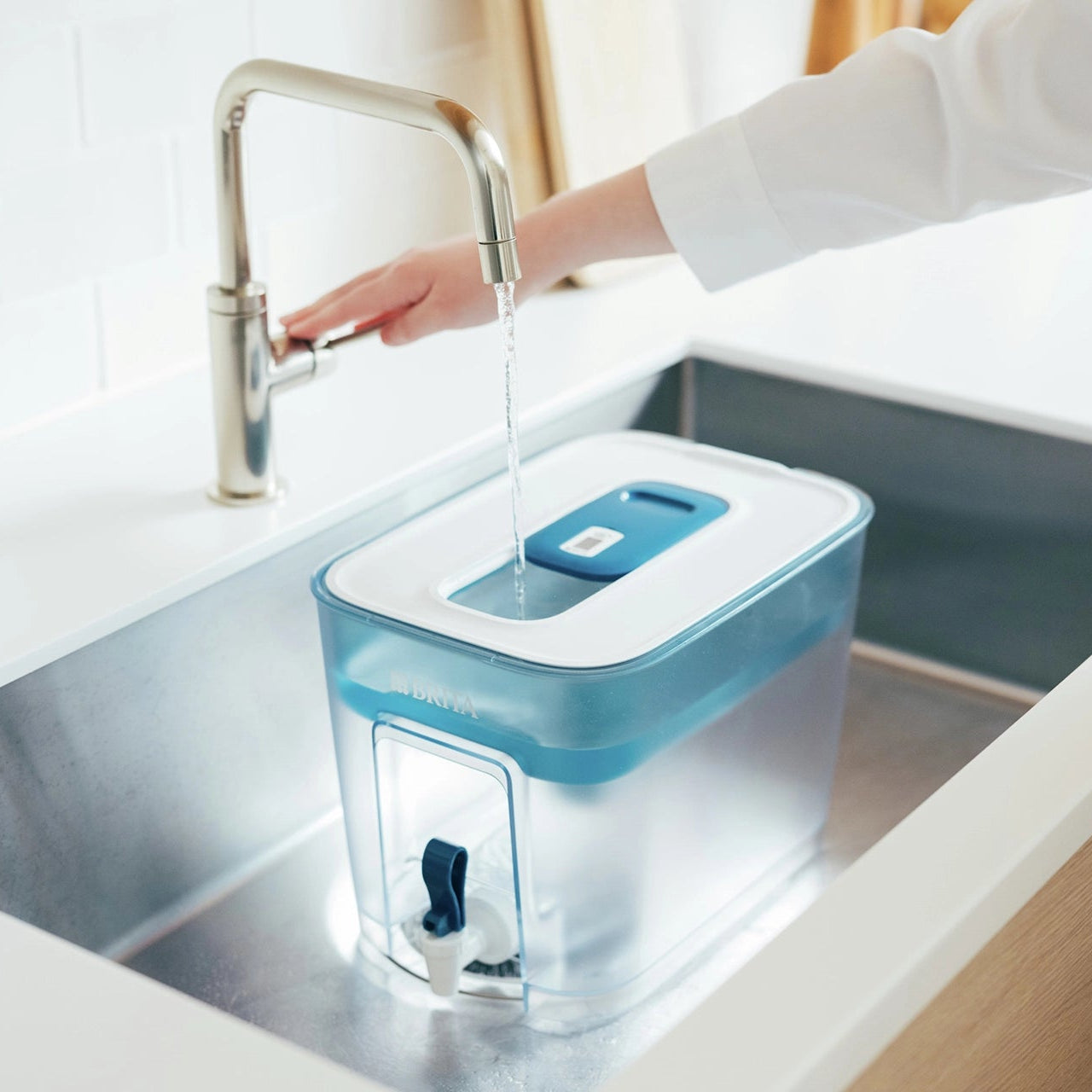 BRITA Flow acqua filtro un contenitore che viene riempito d'acqua nel lavello della cucina sotto un rubinetto aperto.