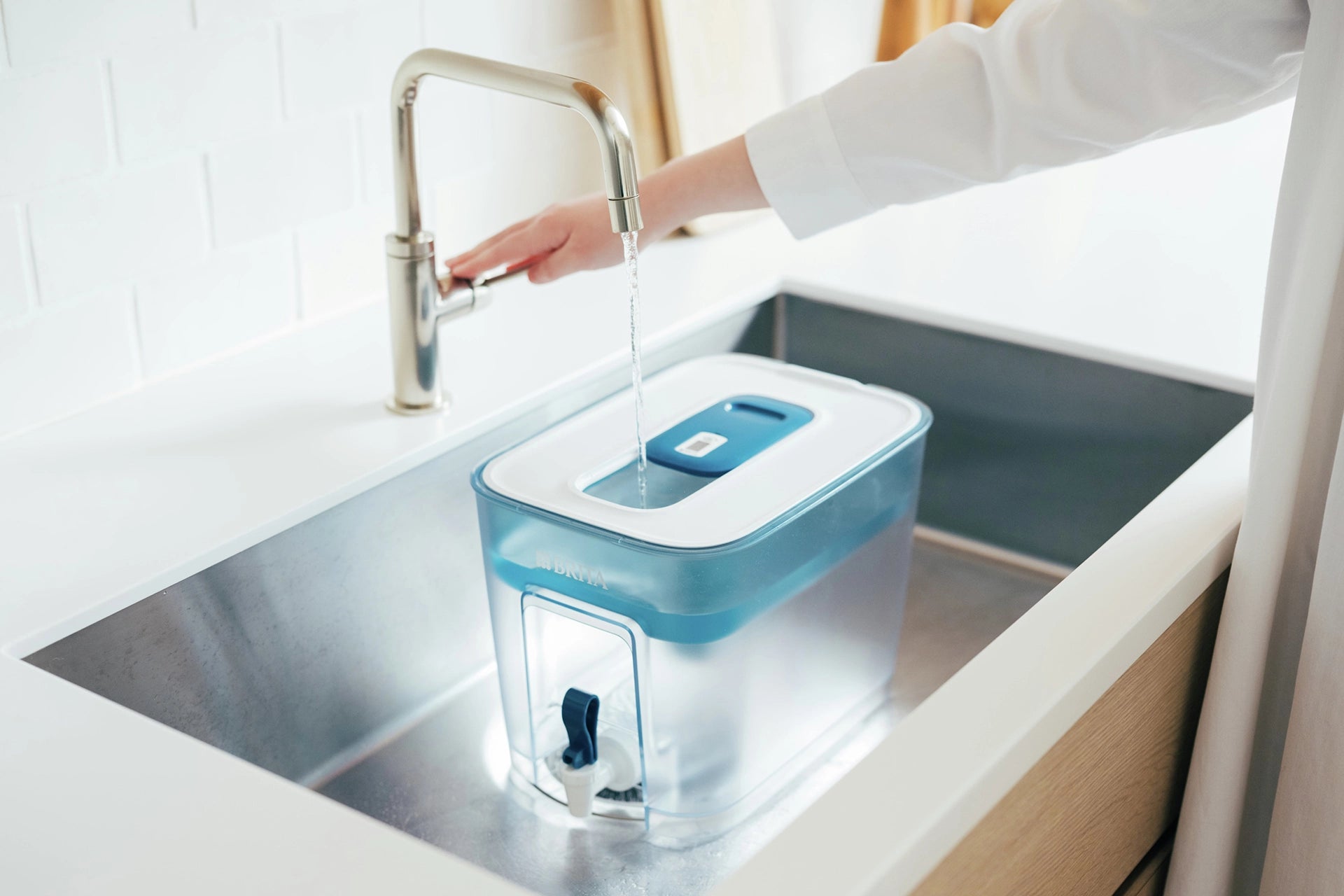 BRITA Flow water filter container being filled with water in a kitchen sink beneath a running tap.