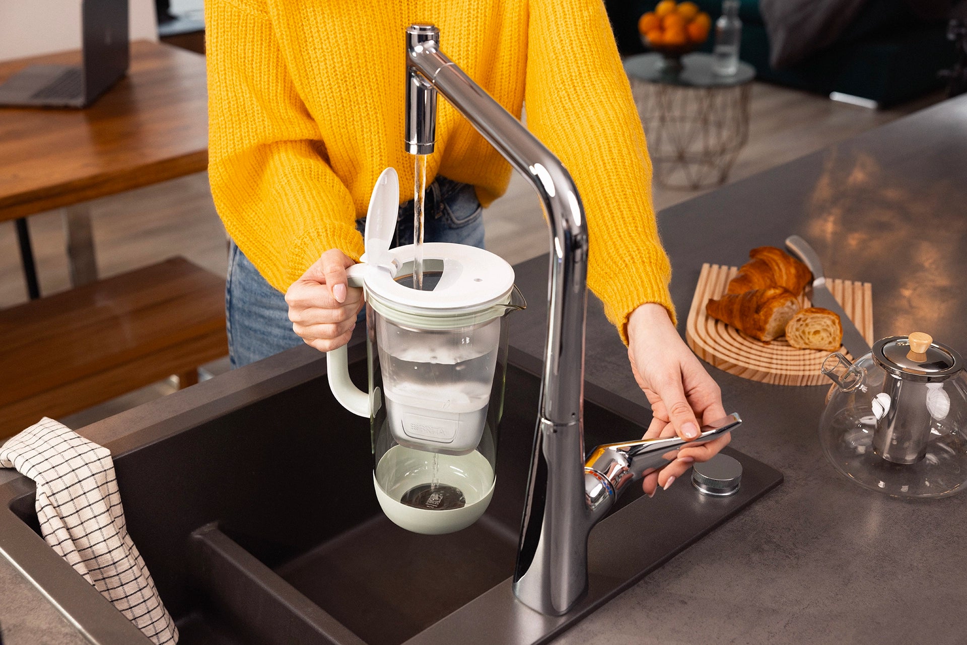 Person filling a green BRITA Glass Jug with tap water at a kitchen sink.