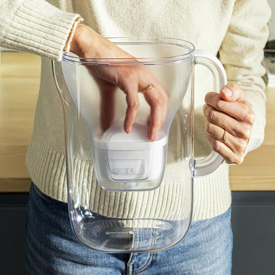 Person in a white sweater inserting a MAXTRA PRO filter cartridge into a BRITA Style Essential water filter jug.