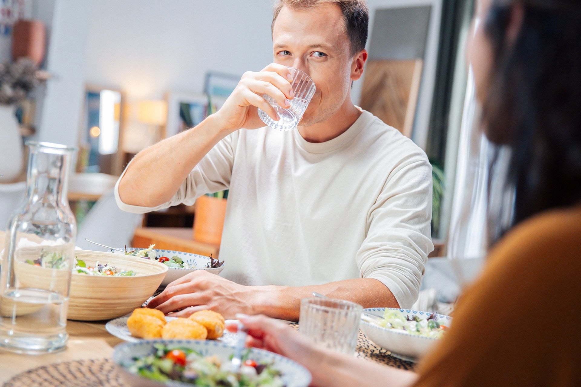 Man drinking water at a dining table with food and another person partially visible