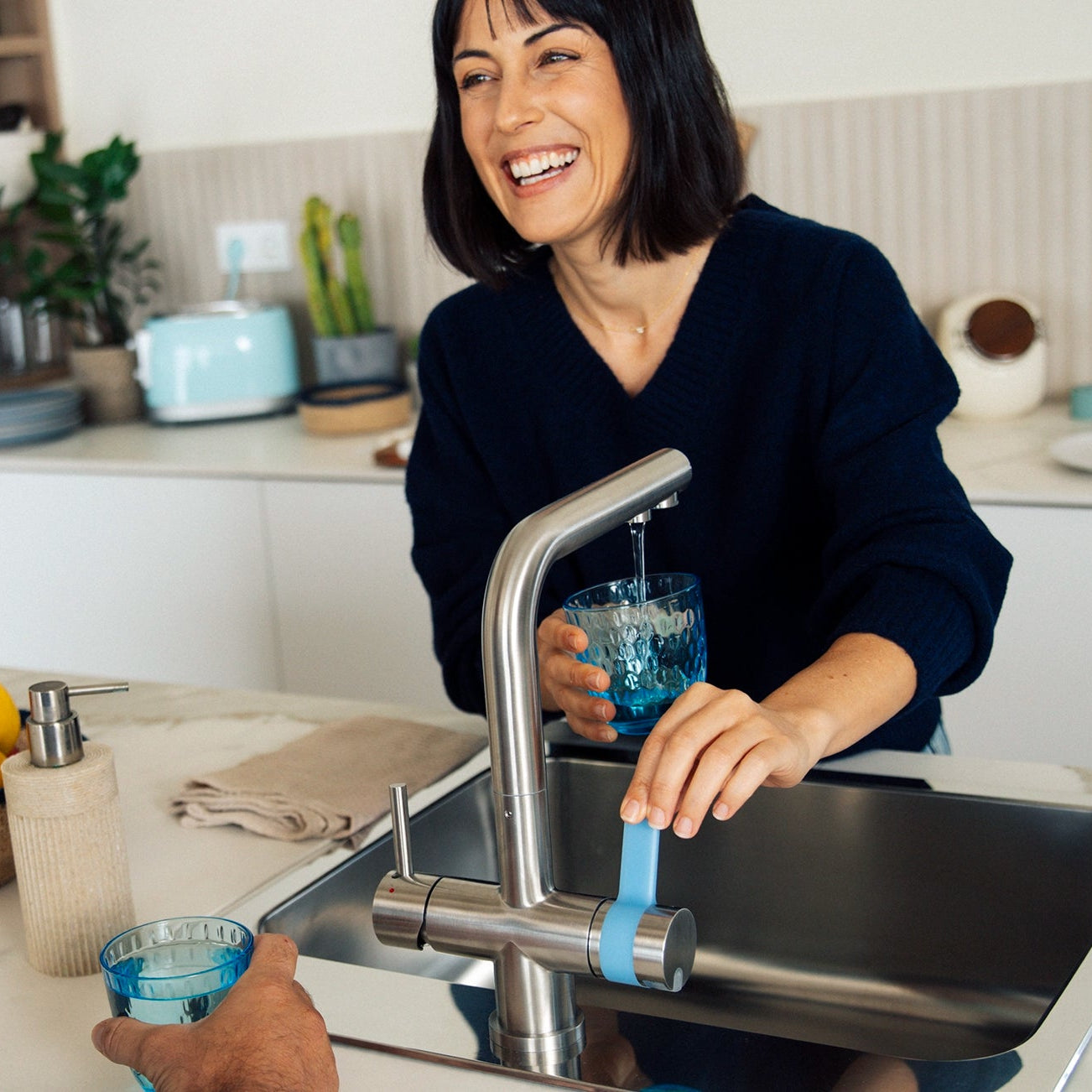 Una donna che versa l'acqua dal filtro BRITA a 3 vie filtro versa un po’ di birra in un bicchiere in cucina, con un uomo in piedi accanto a lei.