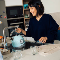 Woman filling a kettle with filtered water from a BRITA 3-way-tap in a modern kitchen.