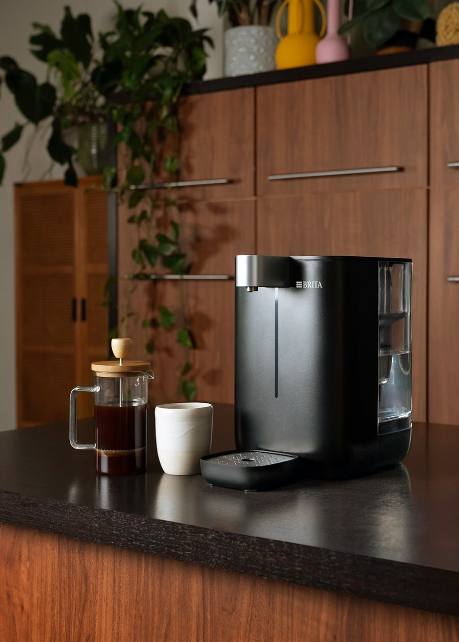 YOURCE mini on a kitchen counter next to a cup and a coffee maker.