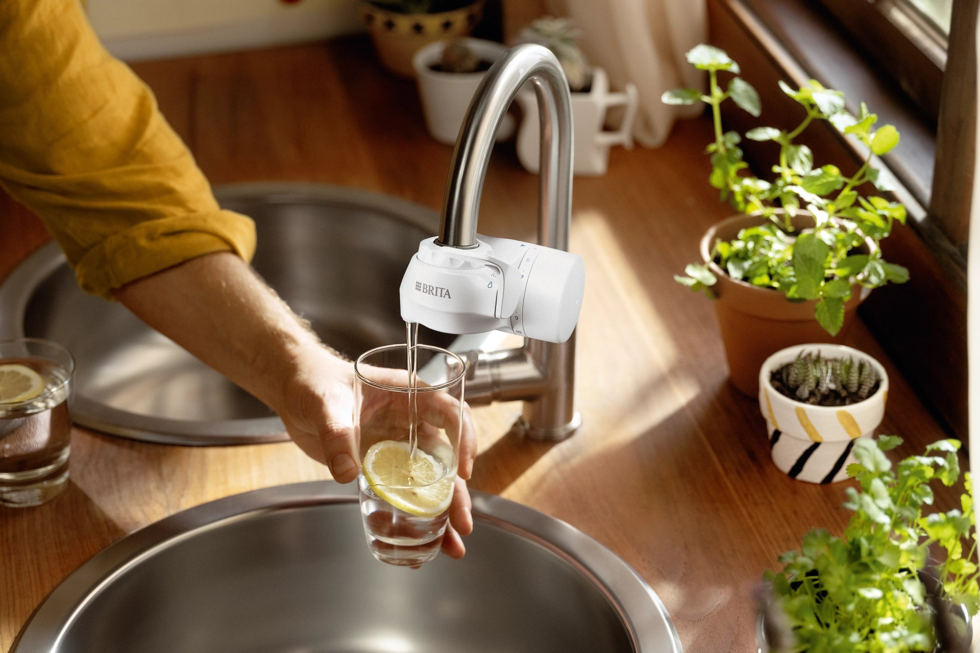Glass with a lemon slice being filled with filtered water from a BRITA ON TAP water filter system.