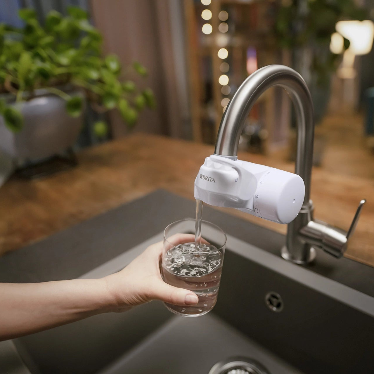 Person filling a glass with filtered water from a BRITA ON TAP water filter.