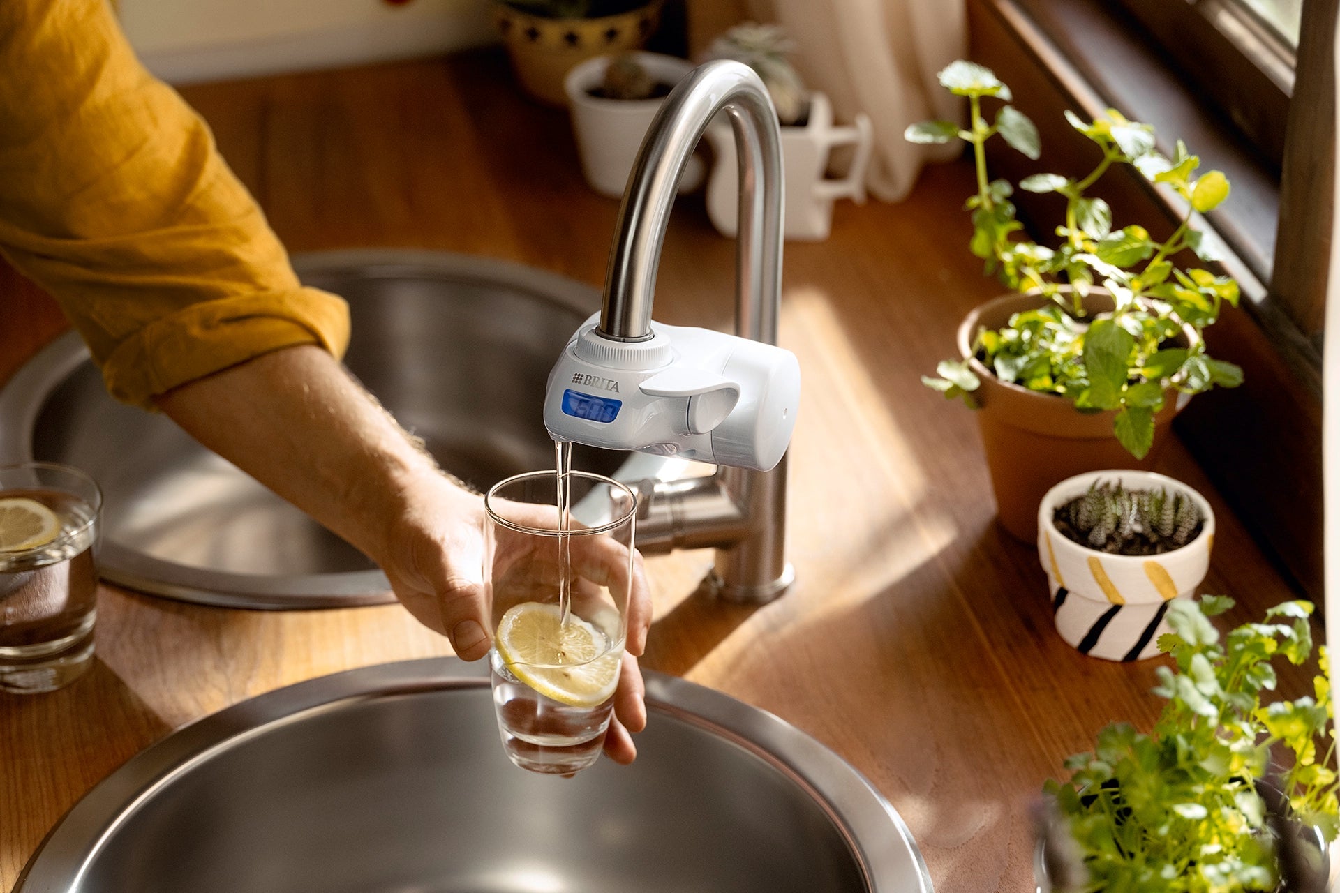 Hand holding a glass with lemon slice being filled from a BRITA tap filter.