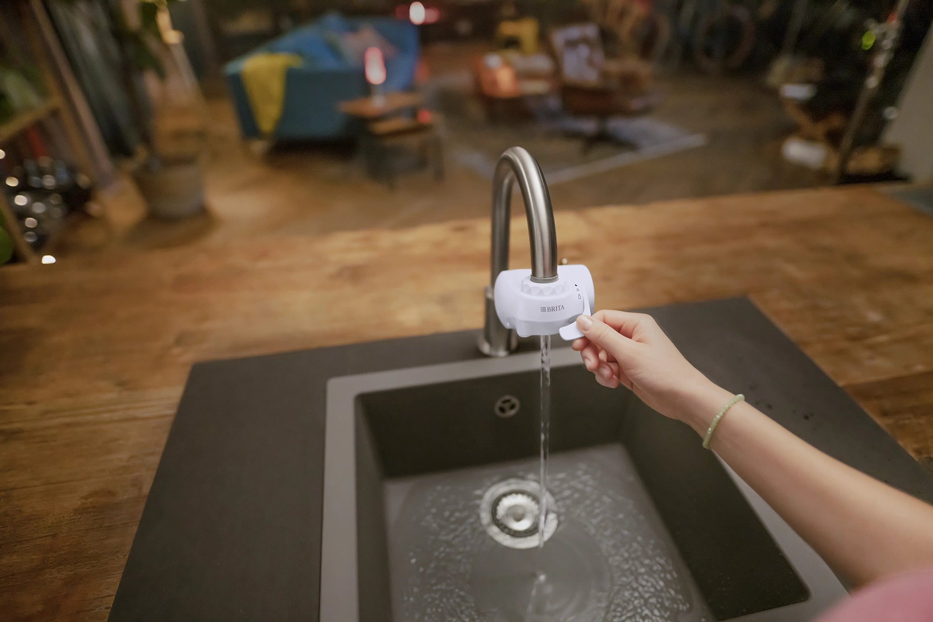 Person using a BRITA ON TAP water filter at a kitchen sink with a blurred indoor background.